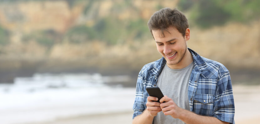 Teen guy using a smart phone on the beach